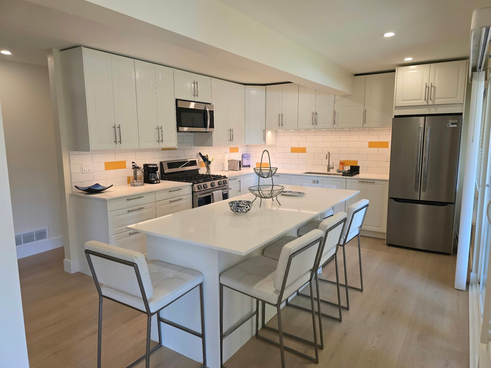 White kitchen with a large island, bar stools, a gas range and a stainless fridge.